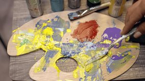 Woman artist is mixing oil paint with a palette knife on a painting palette.