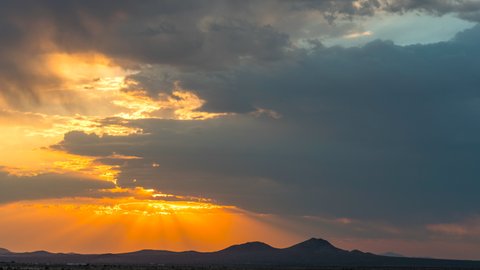 Colorful and dynamic cloudscape with a cloudburst over a mountain range in silhouette at sunrise - static time lapse