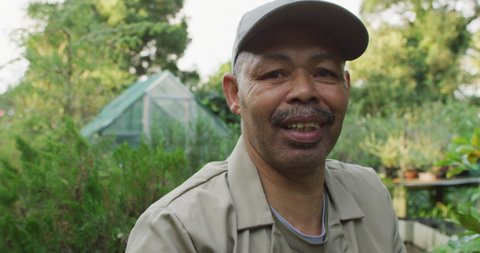 African american male gardener using tablet at garden center, looking at camera and smiling. working at bonsai nursery, small specialist business.
