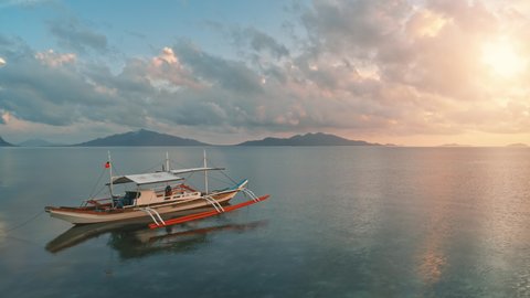 Philippines wooden boat in colorful sunset. Paradise background. Drone low fly over traditional Bangka ship. Pink clouds sky ferlect in calm sea water. Beautiful wild landscape. Exotic summer vacation