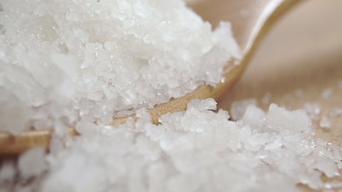 Coarse sea salt pours in and fills the wooden spoon in slow motion. Macro. Natural ingredient and spa mineral
