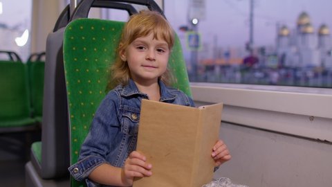 Portrait of attractive young little child girl sitting at empty subway train, reading interesting book. Concept of people, literature, public transport. Kid passenger traveling at modern tram or bus