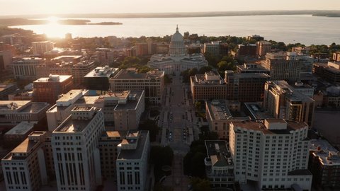 Aerial above the lake towards city street leading to domed Wisconsin State Capitol building in Madison with sun reflect off water of Lake Mendota, Wisconsin. Warm sunset light	