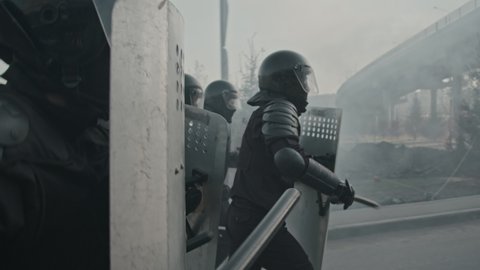 Slowmo tracking shot of riot police officers with shields and batons running after protesters with signs