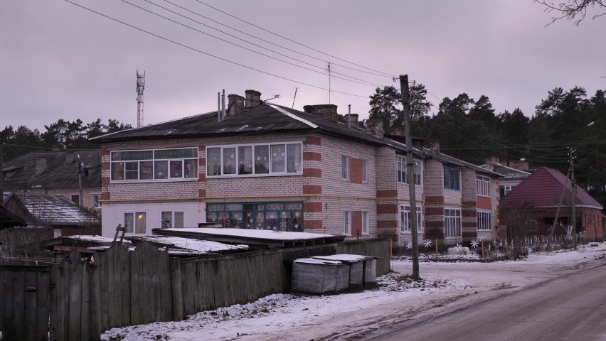 A fence and a road in front of a village building against a sky by winter day
