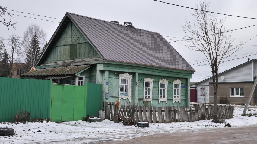 A road and a fence in front of a village wooden house against a sky by winter day