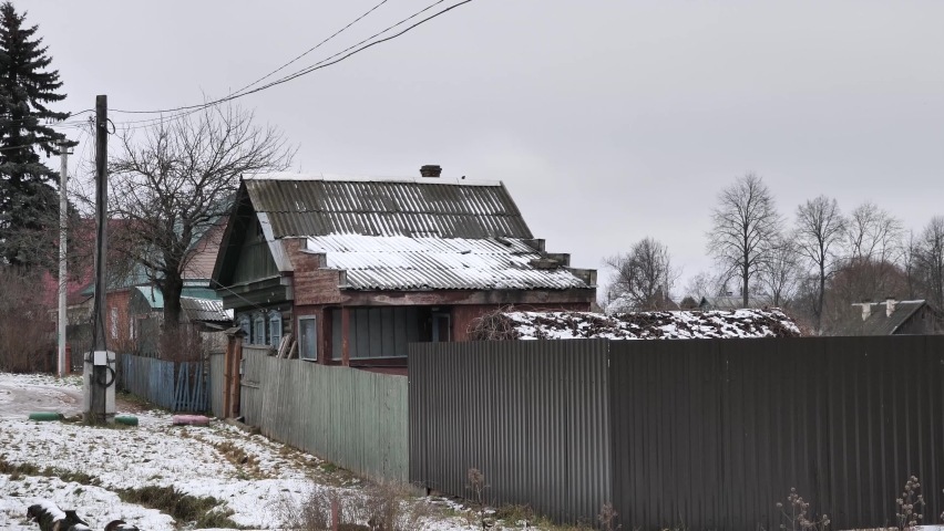 A fence and an overhead electric line in front of a village wooden houses against a sky by winter day