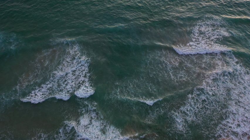 aerial top view sea waves seamless loop on the white Phuket sand beach. 
Wave after wave swept towards the shore at sunset. 
 blue sea, and clear sand landscape. Paradise beach.