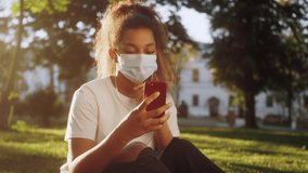 Young black woman wearing protective medical mask making selfie, having video chat with friends during walking in summer park.