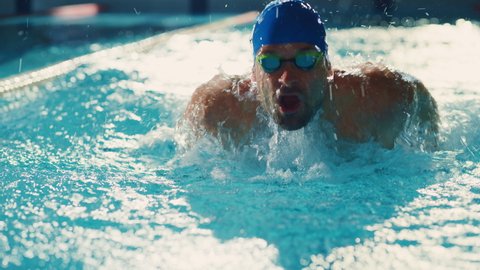 Successful Male Swimmer Racing, Swimming in Swimming Pool. Professional Athlete Determined to Win Championship using Butterfly Style. Colorful Cinematic Shot. Front View Portrait Slow Motion