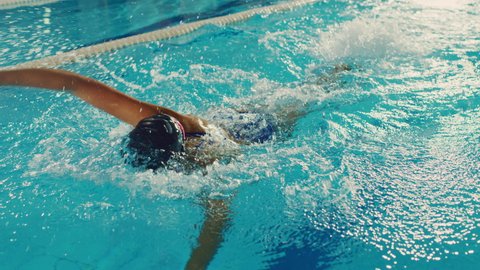 Beautiful Female Swimmer Using Front Crawl, Freestyle in Swimming Pool. Professional Athlete Determined to Win Championship. Cinematic Slow Motion, Stylish Colors, Artistic Tracking Shot