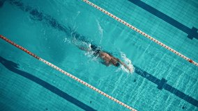 Aerial Top View: Muscular Male Swimmer in Swimming Pool. Professional Athlete Swims in Backstroke Style, Determination in Training to Win Championship. Cinematic Spinning Shot with Stylish Colors - Powered by Shutterstock - Get 15% off with code: PIKWIZARD15