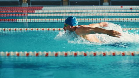 Successful Male Swimmer Racing, Swimming in Swimming Pool. Professional Athlete Determined to Win Championship using Butterfly Style. Colorful Cinematic Shot. Side View Tracking Slow Motion