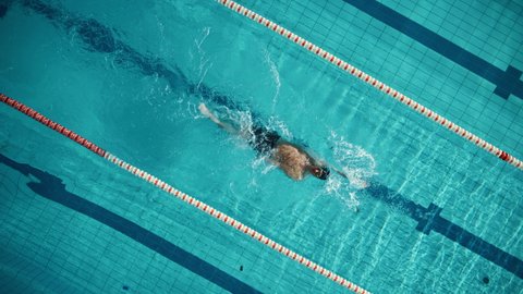 Aerial Top View: Muscular Male Swimmer in Swimming Pool. Professional Athlete Swims in Backstroke Style, Determination in Training to Win Championship. Cinematic Slow Motion, Stylish Colors