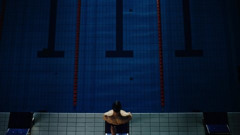 Aerial Top View Male Swimmer Jumps, Dives into Swimming Pool. Professional Athlete Winning World Championship. Dark Dramatic Saturated Colors, Cinematic Light, Artistic Top Down Flyover Slow Motion