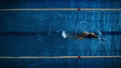 Aerial Top View: Athletic Female Swimmer in Swimming Pool. Professional Athlete Swims in Backstroke Style, Determination to Win Championship. Dark Dramatic Colors, Cinematic Lap Lane Light
