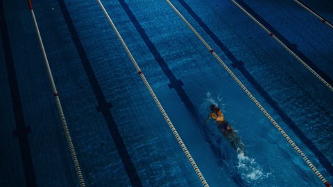 Female Swimmer Racing in Swimming Pool. Professional Athlete Determined to Win Championship using Butterfly Style. Dark Dramatic Colors, Cinematic Lap Lane Light. Aerial Static Lock Dutch Angle Shot