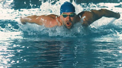 Successful Male Swimmer Racing in Swimming Pool. Professional Athlete Determined to Win Championship using Butterfly Style. Colorful Cinematic Shot. Front View Portrait Slow Motion