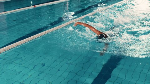 Beautiful Female Swimmer Using Front Crawl, Freestyle in Swimming Pool. Professional Athlete Determined to Win Championship. Cinematic Slow Motion, Stylish Colors, Artistic Tracking Wide Shot