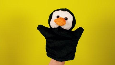 Soft puppet toy on yellow background. Concept of puppet show. Close-up of puppet penguin