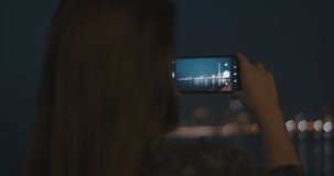 Close up of a young woman using a smartphone to take pictures of a night cityscape. Slow motion, close up.