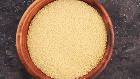 Raw couscous cereal seeds in wooden plate stir with eco friendly spoon on dark background