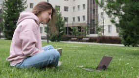 Young woman, in park on the grass, learning to watch online webinar, webcast class, looking at distance e-learning course for laptop or teacher by video link with webcam