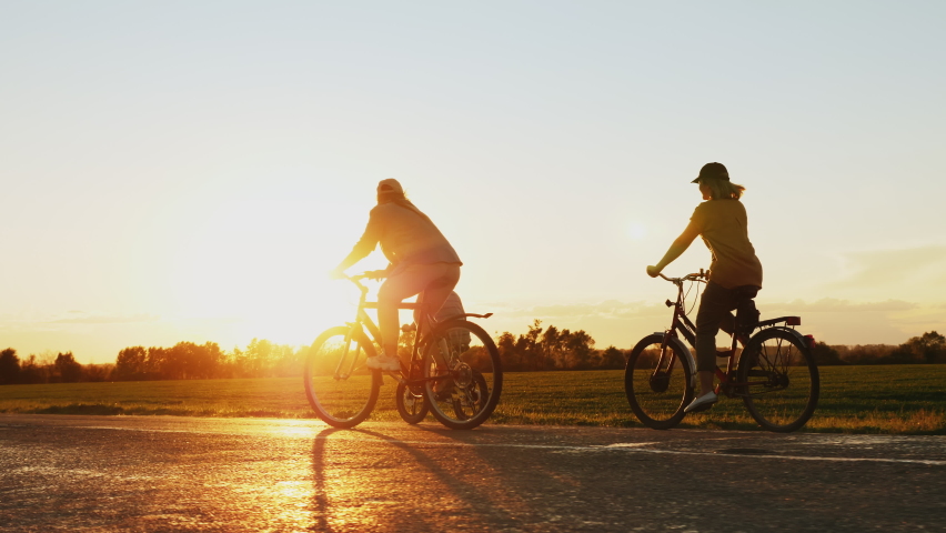 Mother with her teenage daughter and little son traveling on bicycles on a country road at sunset