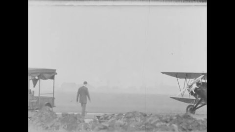 CIRCA 1930 - Pilots check their planes on an airfield, and one takes off in a biplane.