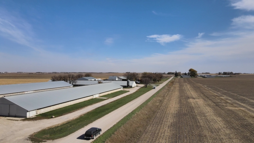 IOWA - CIRCA 2020s - Aerial drone footage of a black SUV on a farm road passing farm buildings under the blue skies of rural, midwestern Iowa.