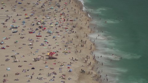 NAZARE, PORTUGAL – 12 JUNE 2021: Large waves crash on beach of Nazare, as people prepare for the Summer holiday after coronavirus lockdown measures were eased in Portugal
