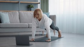 Online Gym. Sporty Senior Female Exercising At Laptop Computer Standing In Plank Position Training In Living Room At Home. Distance Fitness, Sport Routine And Motivation In Older Age