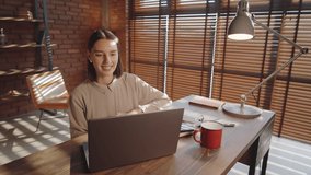 Arc shot of young beautiful business lady smiling, waving and speaking on online video call on laptop while working in office