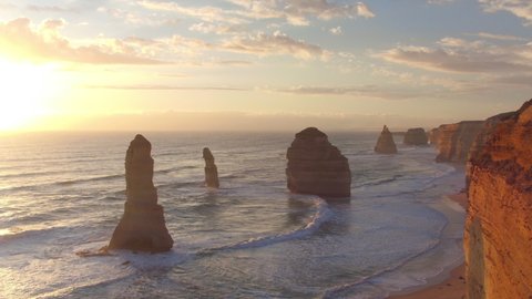 AERIAL: Golden sunshine illuminates the cliffs and other rock formations on coast of Australia. Spectacular drone point of view of the famous 12 Apostles beach in Australia on a sunny summer evening.