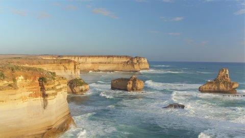 AERIAL: Blue ocean waves roll towards the breathtaking cliffs of Twelve Apostles in Victoria. Cinematic drone point of view of a spectacular limestone coastline in Australia. Tourist attraction.