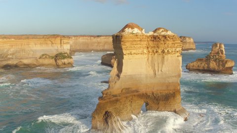 AERIAL: Cinematic drone point of view of a spectacular limestone coastline in Australia. Blue ocean waves roll towards the breathtaking cliffs of Twelve Apostles in Victoria. Tourist attraction.