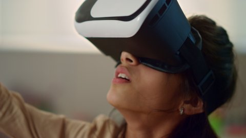 Portrait of focused girl wearing virtual reality headset at school lesson. Cheerful schoolgirl exploring cyberspace with virtual glasses. Multi ethnic child immersing in virtual reality at school