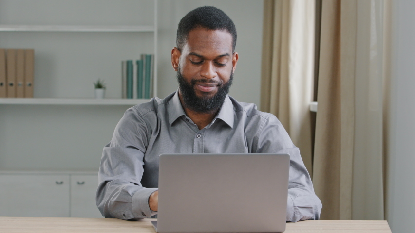 Young office worker working overtime performing urgent assignment preparing report typing on laptop, taking short break, pause. African american modern writer journalist prepares article writes novel Royalty-Free Stock Footage #1075130018
