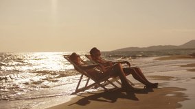 Man and woman relaxing in loungers on beach in late afternoon sun. Waves washing sand. Summer at seaside. - Powered by Shutterstock - Get 15% off with code: PIKWIZARD15