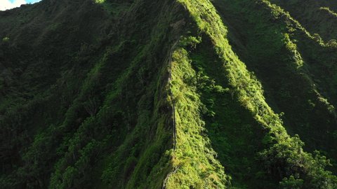 Aerial Moving Towards A Hikers Climbing A Mountain Ridge Hiking Trail Stairway, With Rough Terrain And Lush Green Slopes - Oahu, Hawaii