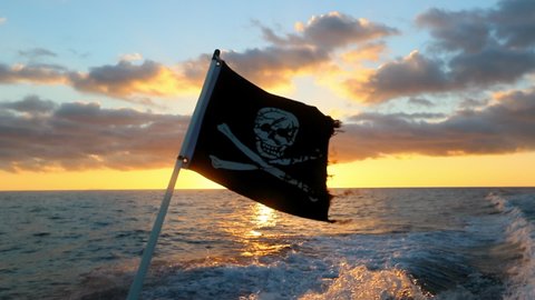 Close-Up Slow Motion Shot Of Skull And Crossbones Symbol Flag Waving During Sunset Against Orange Cloudy Sky - Kauai, Hawaii