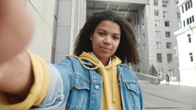 POV portrait of cheerful mixed race woman with curly hair chatting and waving hand making video call outside in city