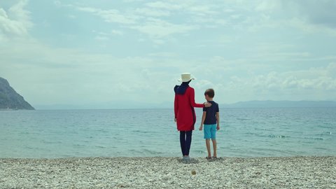 A young woman in a hijab swimsuit and straw hat swims in the sea with her young son. Beautiful and peaceful holiday concept. 