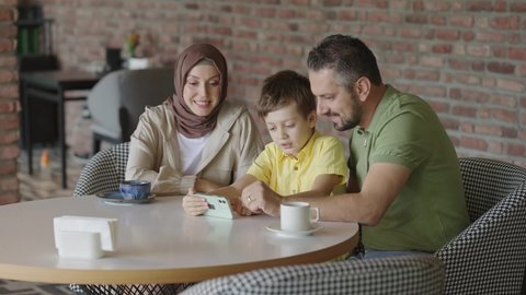 Young woman in hijab and her family are playing games on their smartphones in a cafe. Spending time with family, having fun concept.
