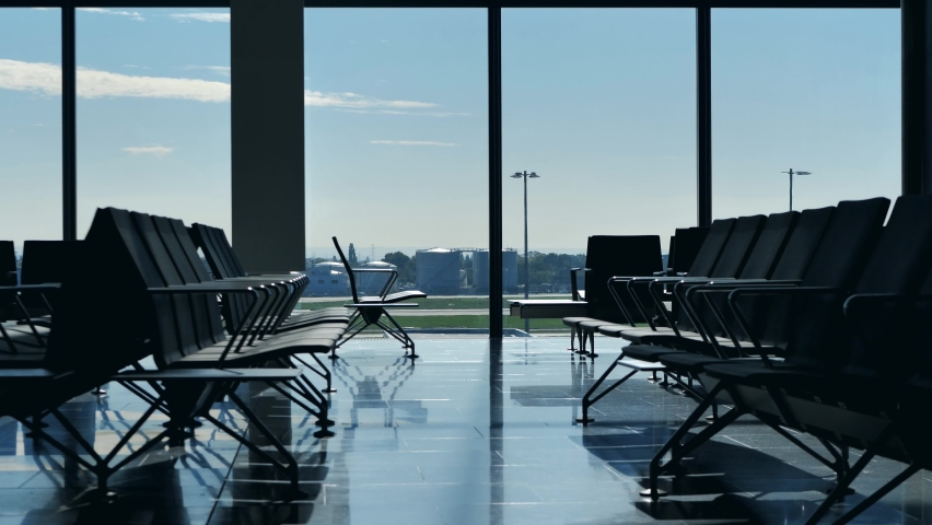Airplane taking off seen through airport terminal window. View from inside empty waiting hall benches with no people in the lounge. Airplane departing with nobody at the gate. Royalty-Free Stock Footage #1075144439