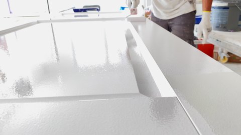 Painter at work paints the wooden door with white paint with a paint roller.  Professional painting services
