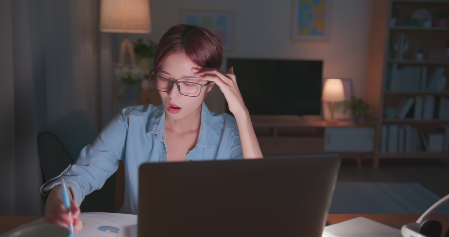 Tired young freelance worker rubbing her eyes while sitting in front of laptop computer and working on promising project - asian girl soho lady stay up late in home office holding glasses eye painful | Shutterstock HD Video #1075154192