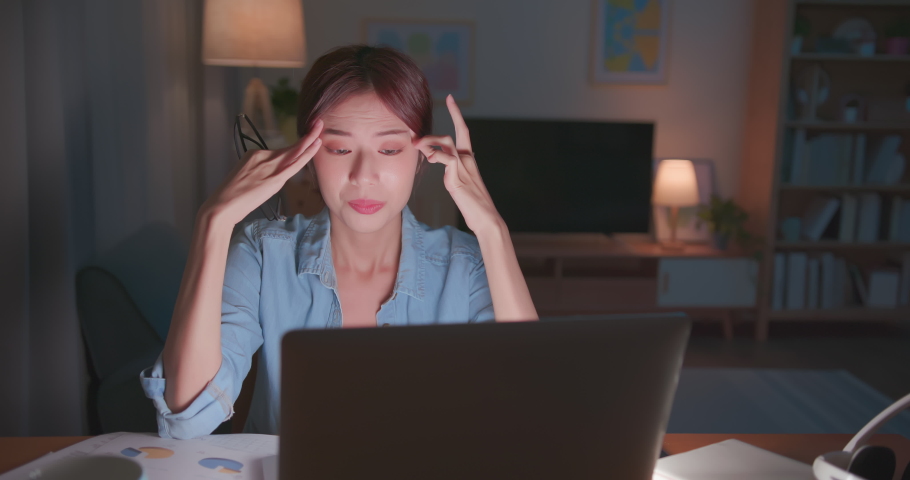 Tired young freelance worker rubbing her eyes while sitting in front of laptop computer and working on promising project - asian girl soho lady stay up late in home office holding glasses eye painful | Shutterstock HD Video #1075154192