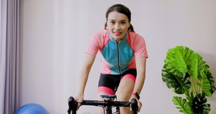 asian woman exercising on stationary bike - bicyclist teacher filming bicycle online class on video for social media at home during coronavirus pandemic