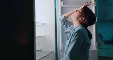 asian woman looking at empty shelf in fridge and she feel upset at night
